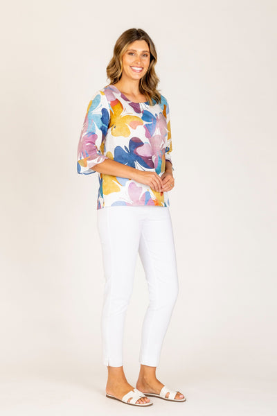 Maglia Butterfly Linen Top with multicolor butterfly print, elbow-length ruffle sleeves, styled with white pants and slide sandals.