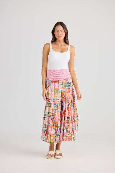 Front view – Model wearing the Pier Skirt in Sardinia Summer print styled as a skirt, with a white tank top and flat sandals.