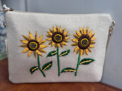 Close-up of neutral woven clutch with hand-beaded sunflower embroidery and green leaf detailing by Anna Nova, available at Binny Bowe Boutique.