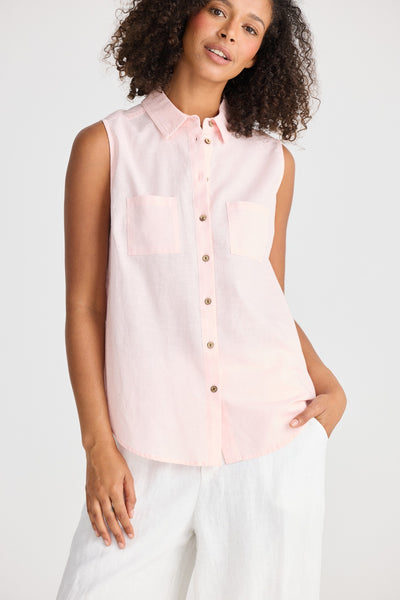 Model wearing the Bazzar Top in pink, sleeveless button-up with collar and patch pockets, styled with white pants.