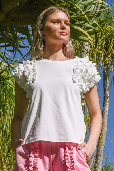 Model wearing the Coop Ruffle Energy T-Shirt in white, featuring dramatic poplin ruffle sleeves, photographed outdoors in bright natural light.
