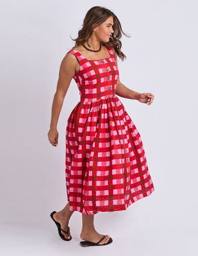 Side view of model wearing the Elm Edin Sleeveless Dress in pink and red check, showing skirt movement.