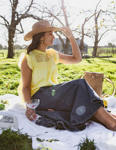 Woman wearing Foxwood Adelyn Top Yellow styled with wide brim hat and denim skirt, picnic scene