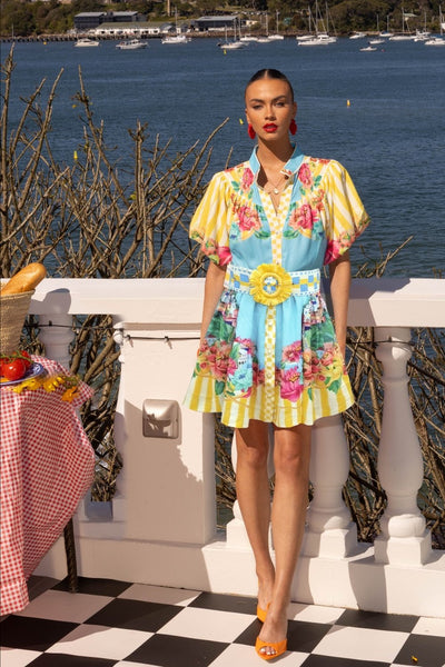 Model wearing the Mia Milani Positano Mini Dress in Aqua Lemon, featuring floral and stripe print with lemon buckle belt, available at Binny Bowe Boutique.