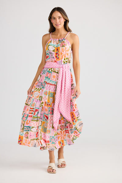 Front view of Pinata Dress Sardinia Summer – Holiday – Model wearing a vibrant, multi-print midi dress with gathered neckline, rope shoulder straps, waist tie, and tiered skirt